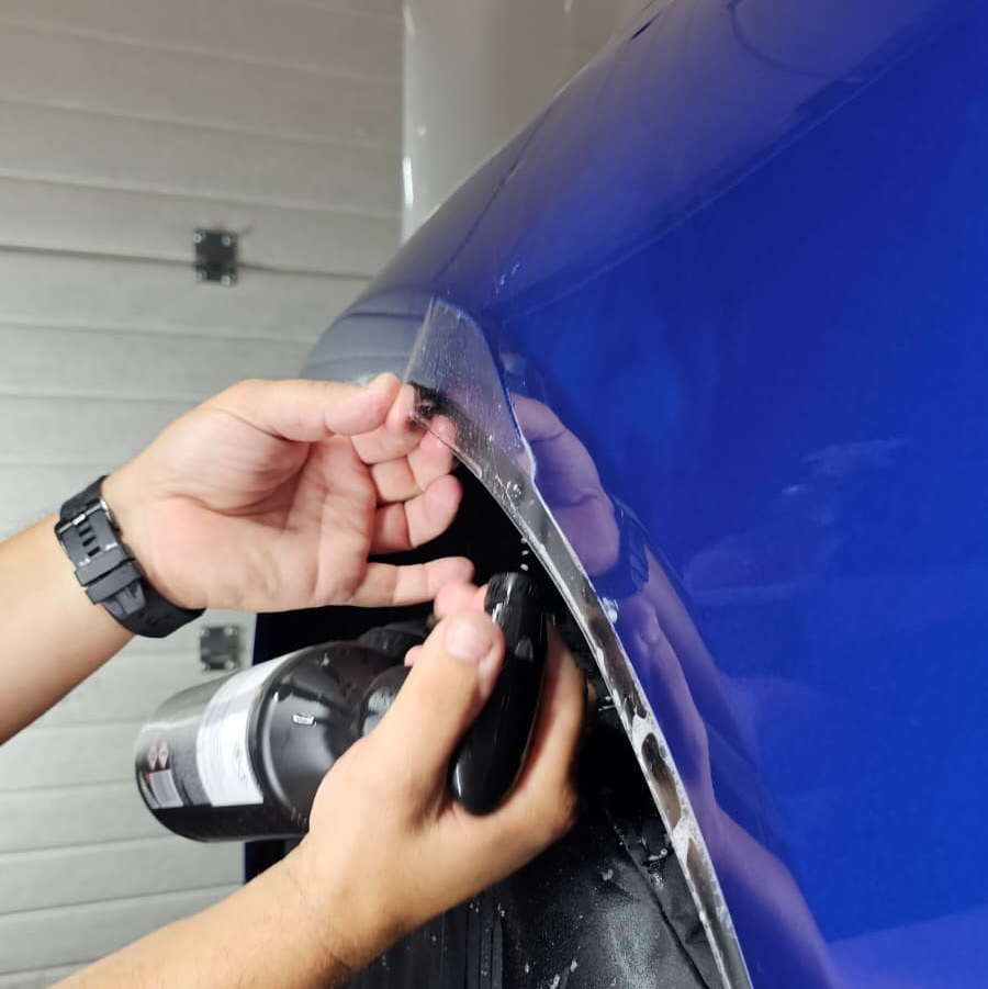 Osoba nanosi zaštitni film na rub plavog automobila unutar garaže.