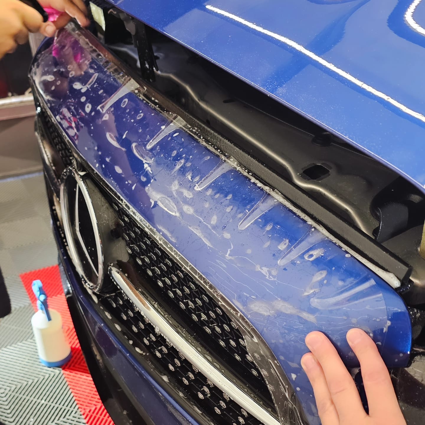  Prednja maska plavog automobila s nanesenim zaštitnim filmom, kapima vode i alatima.